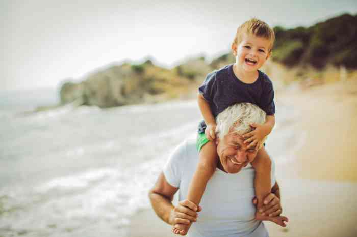 a grandfather holding his grandson on his shoulders at the beach
